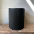 Indlæs billede i gallerivisning, Billede af en rund, sort krukke i moderne design fra DECOPLANTs LIGHT-serie, Ø35 x H40 cm, med matte overflade og lodrette riller, egnet til både indendørs og udendørs brug.